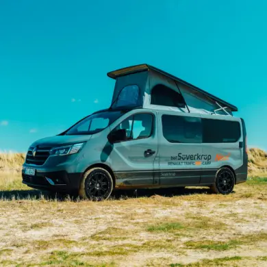 Renault Trafic BS-Camp Campervan mit geöffnetem Aufstelldach steht auf einer Wiese unter blauem Himmel