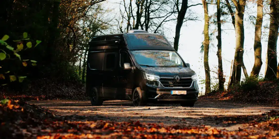 Renault Trafic BS-CAMP Campervan fährt auf einem Laub bedeckten Weg durch herbstlichen Wald.