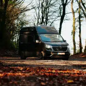 Renault Trafic BS-CAMP Campervan fährt auf einem Laub bedeckten Weg durch herbstlichen Wald.
