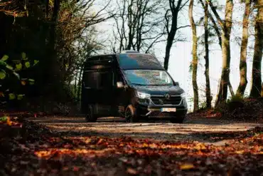 Renault Trafic BS-CAMP Campervan fährt auf einem Laub bedeckten Weg durch herbstlichen Wald.