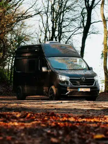 Renault Trafic BS-CAMP Campervan fährt auf einem Laub bedeckten Weg durch herbstlichen Wald.