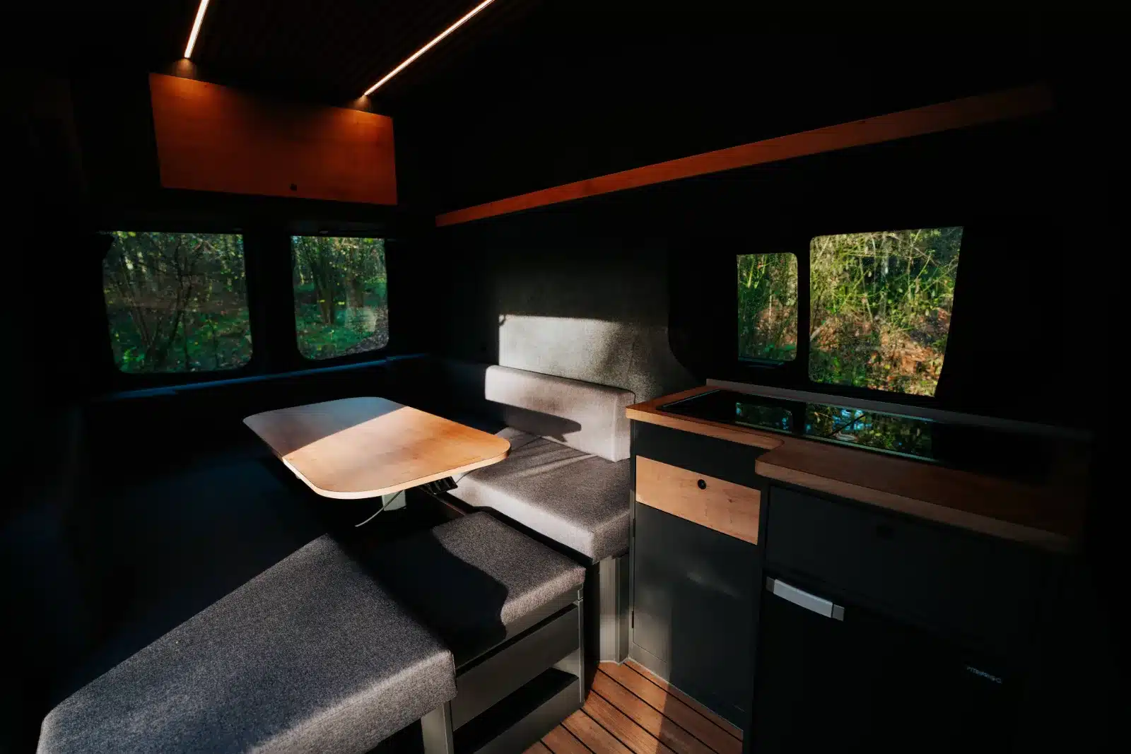 Wohn- und Essbereich des Renault Trafic BS-CAMP mit Sitzbank, Tisch und Küchenzeile.