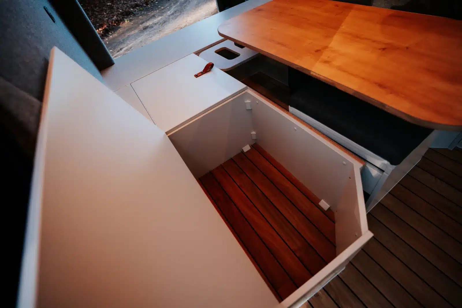 Großes Staufach mit Holzoptik im Wohnbereich des Renault Trafic BS-CAMP, daneben Tisch und Sitzbank