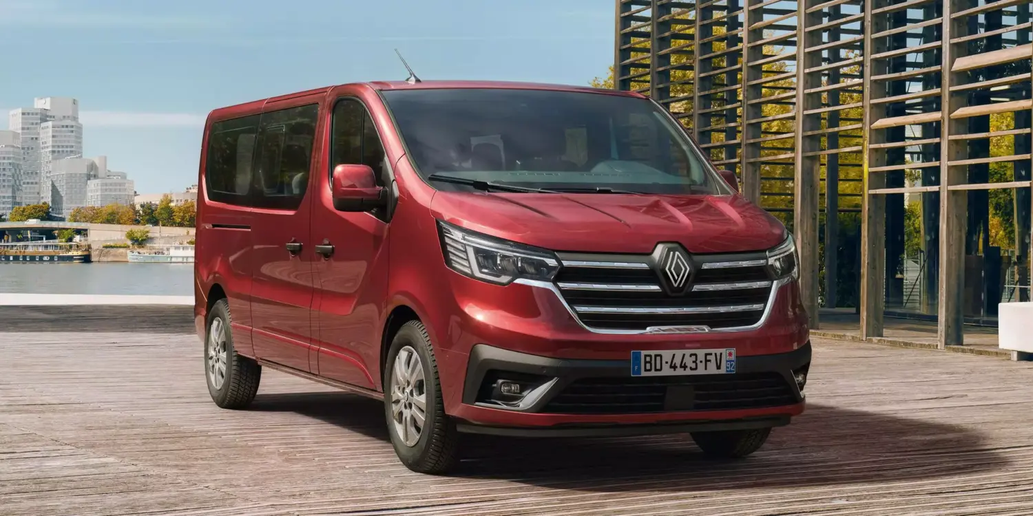 Roter Renault Trafic parkt vor moderner Architektur und Wasser im Hintergrund.
