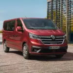 Roter Renault Trafic parkt vor moderner Architektur und Wasser im Hintergrund.