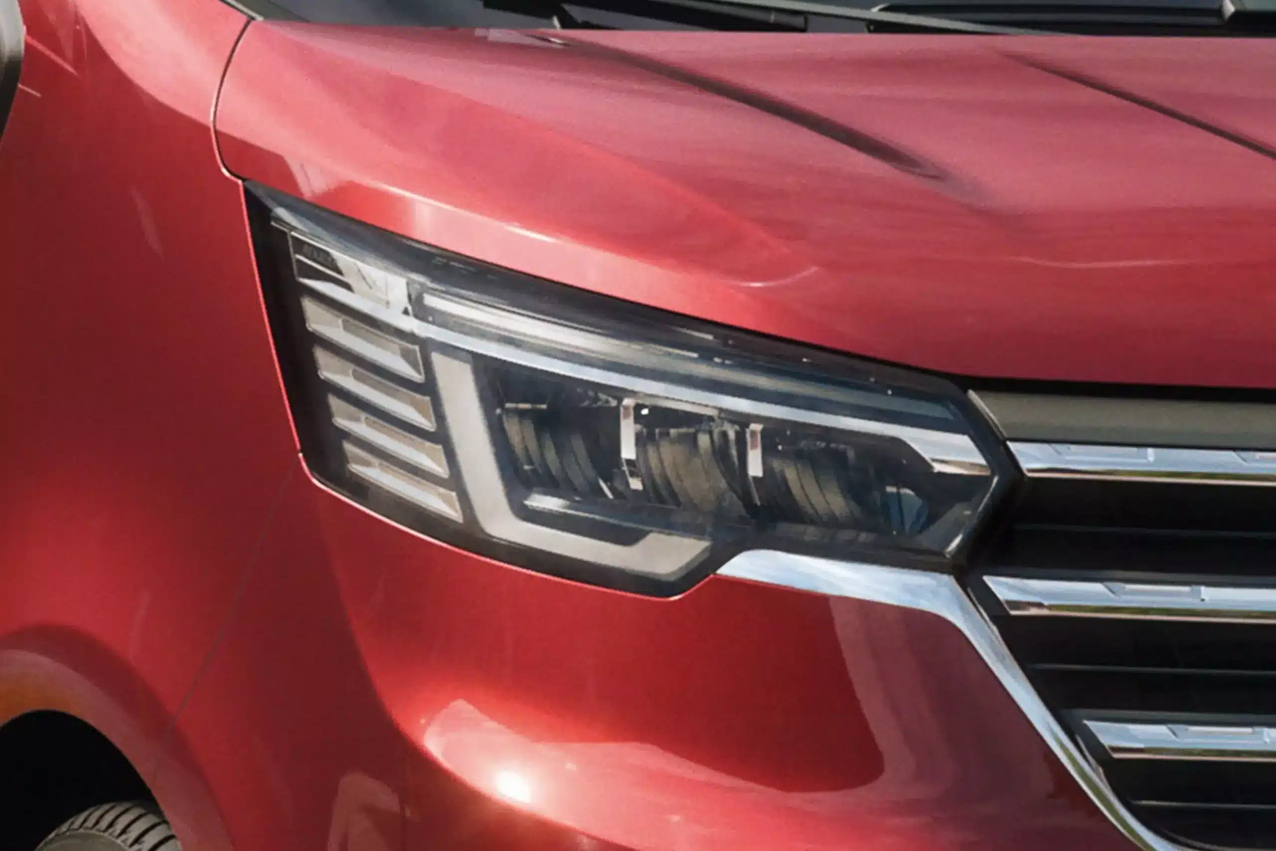 Detailansicht des Frontscheinwerfers eines roten Renault Trafic mit modernem Design.