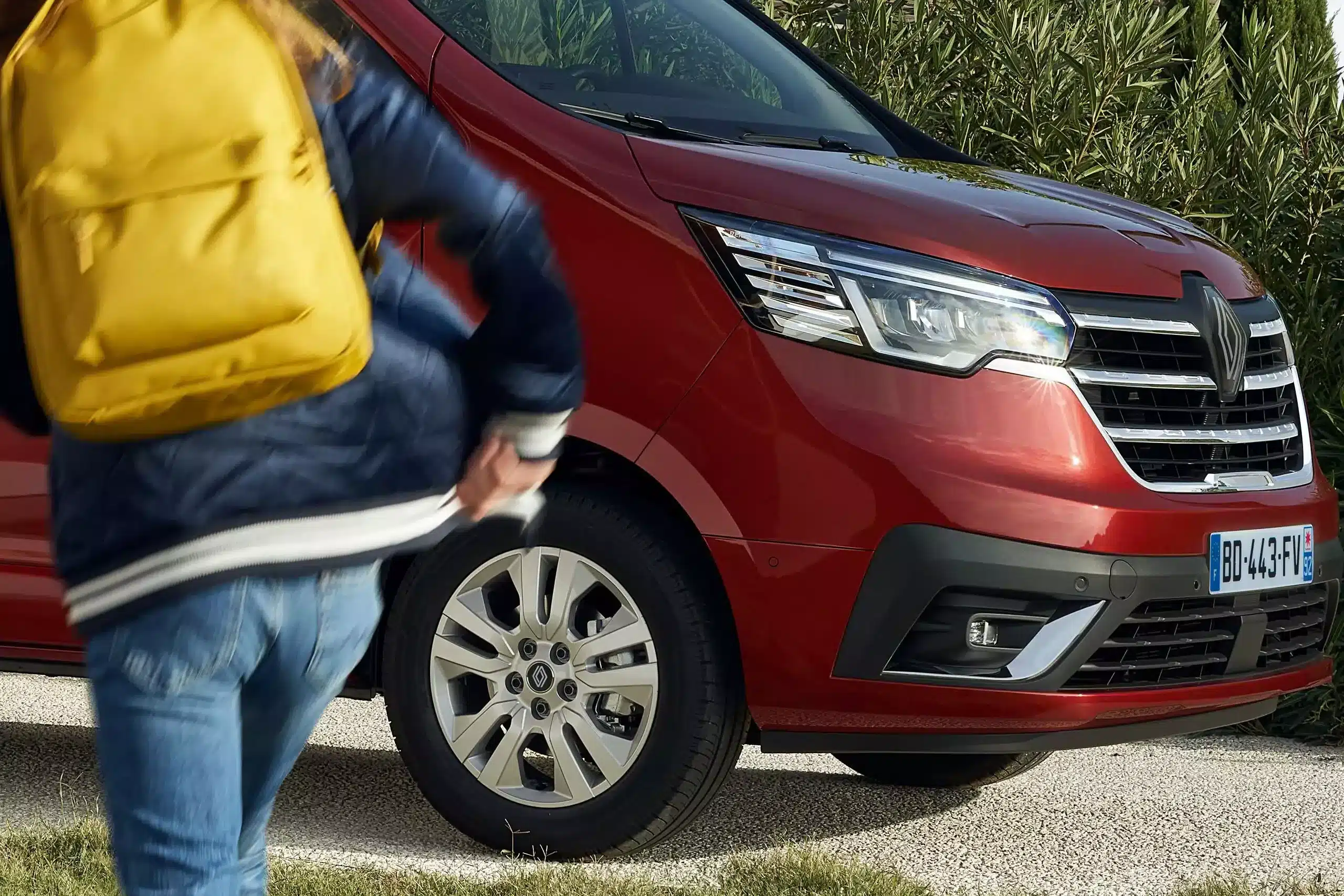 Rote Renault Trafic Front mit modernem Scheinwerferdesign und Person mit gelbem Rucksack