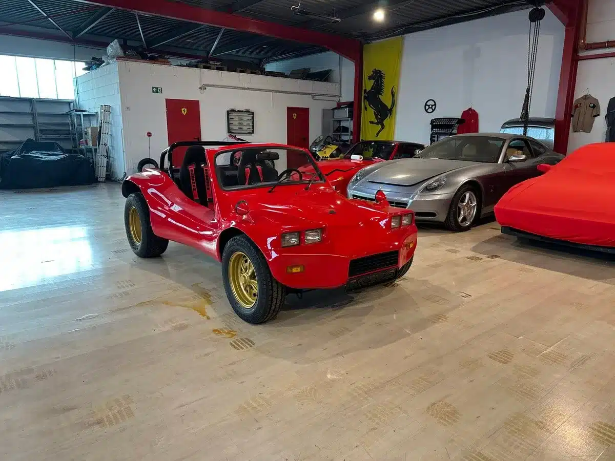 Roter Volkswagen Deserter GT Buggy von 1970 mit goldenen Felgen, stehend in einer Halle mit weiteren Sportwagen.