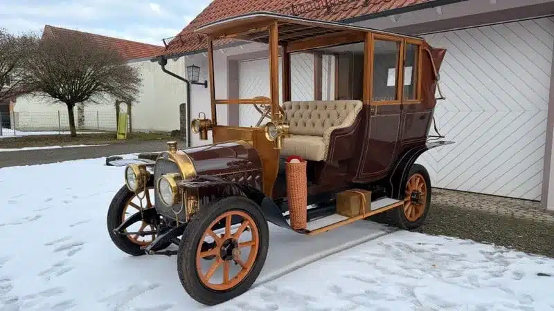 Klassischer Oldtimer mit Holzrahmen und edlen Details, stehend auf verschneitem Hof vor einer Garage