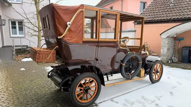 Ein klassisches Automobil aus der Frühzeit des Automobilbaus, gepflegt und detailreich erhalten, geparkt auf einem Hof im Winter.