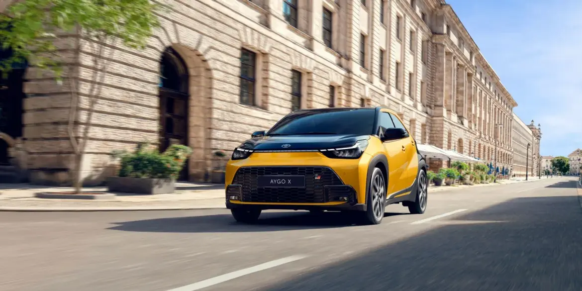 Toyota Aygo X Hybrid in Gelb fährt durch eine Innenstadt mit historischen Gebäuden