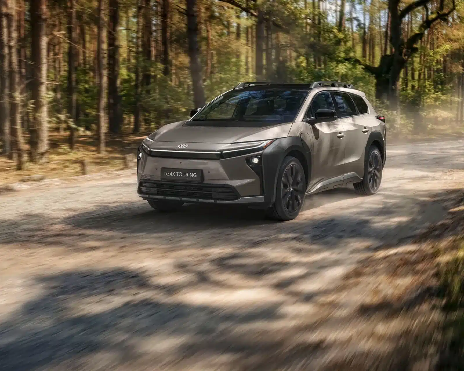 Toyota bZ4X Touring SUV fährt durch einen Wald auf einem staubigen Weg.