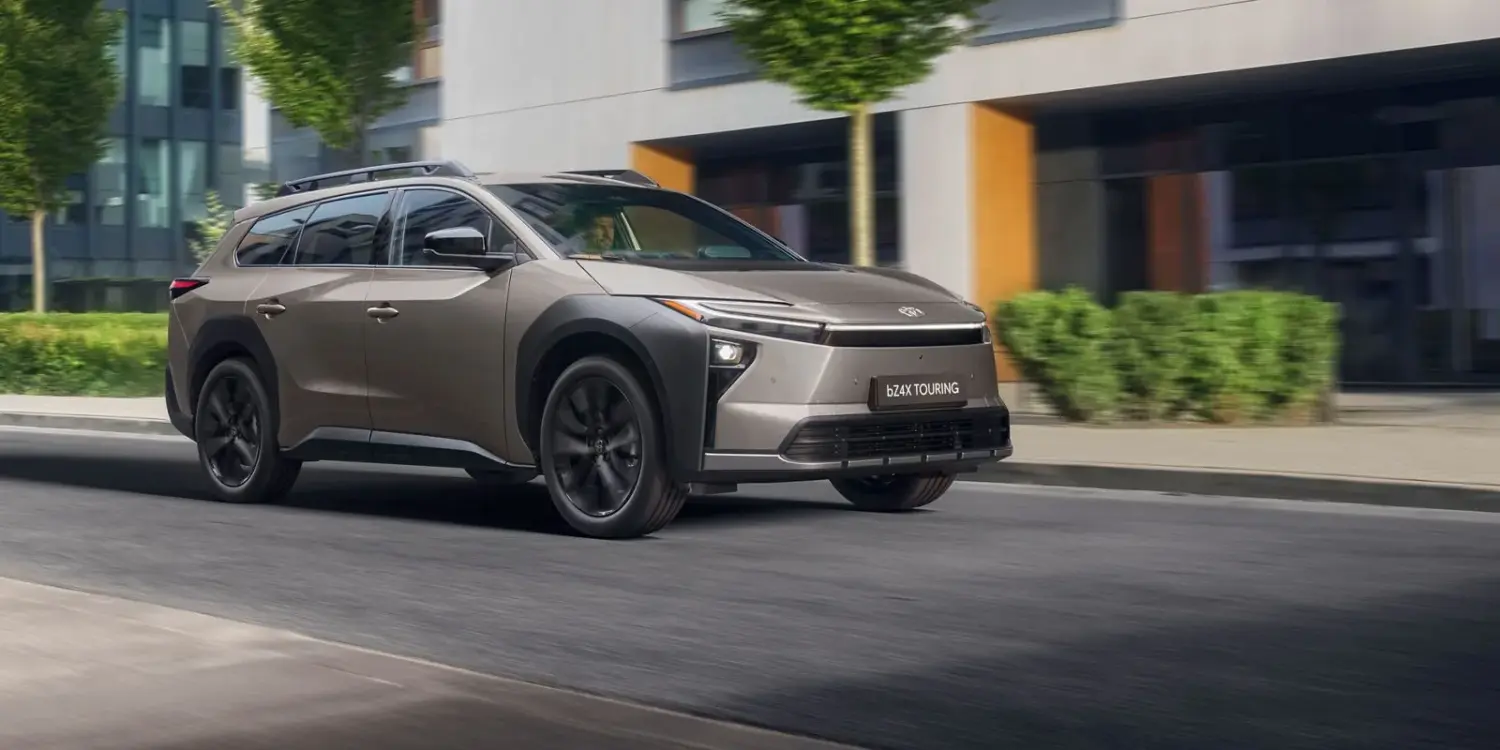 Toyota bZ4X Touring Elektro-SUV bei der Fahrt durch eine Stadt mit Bäumen und modernen Gebäuden im Hintergrund