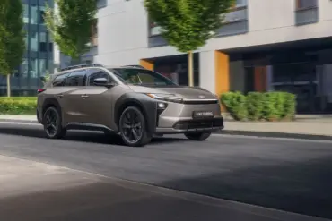 Toyota bZ4X Touring Elektro-SUV bei der Fahrt durch eine Stadt mit Bäumen und modernen Gebäuden im Hintergrund