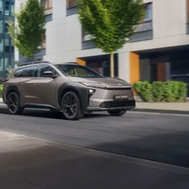 Toyota bZ4X Touring Elektro-SUV bei der Fahrt durch eine Stadt mit Bäumen und modernen Gebäuden im Hintergrund