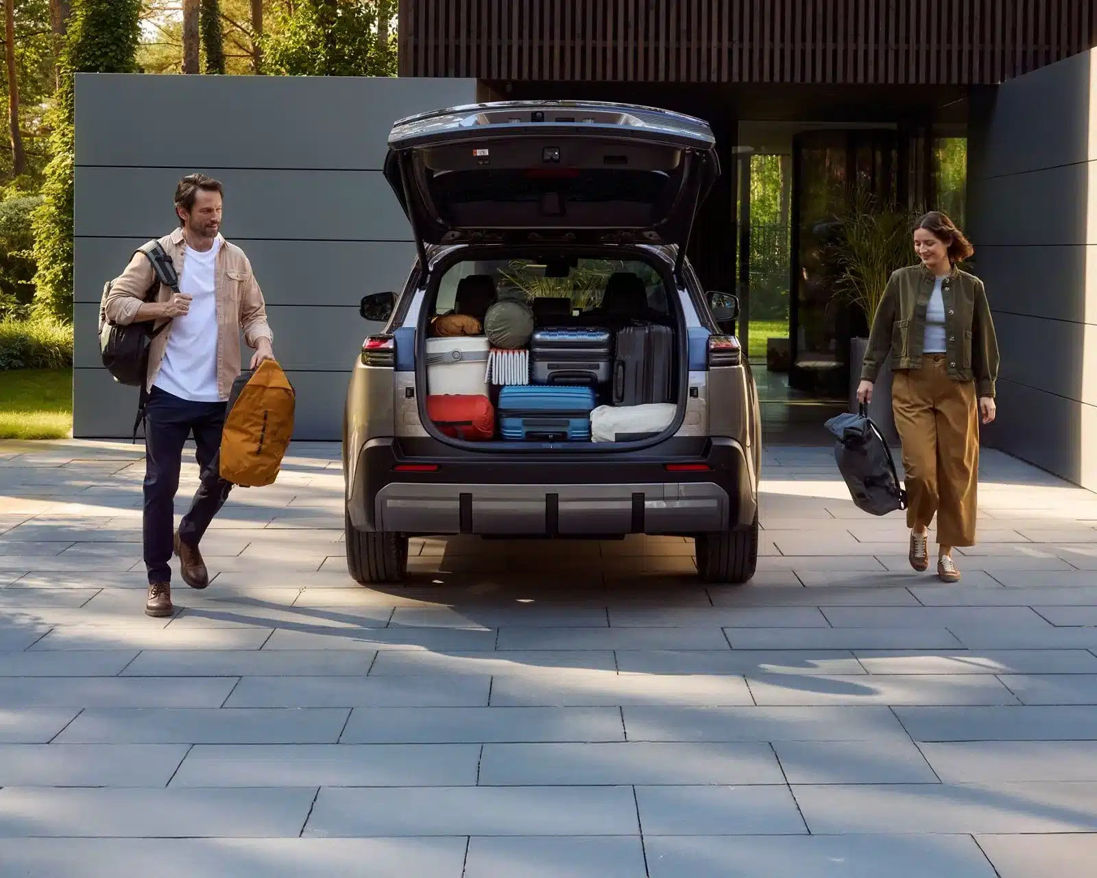 Toyota bZ4X Touring mit offenem Kofferraum, beladen für einen Ausflug, davor zwei Personen mit Taschen.