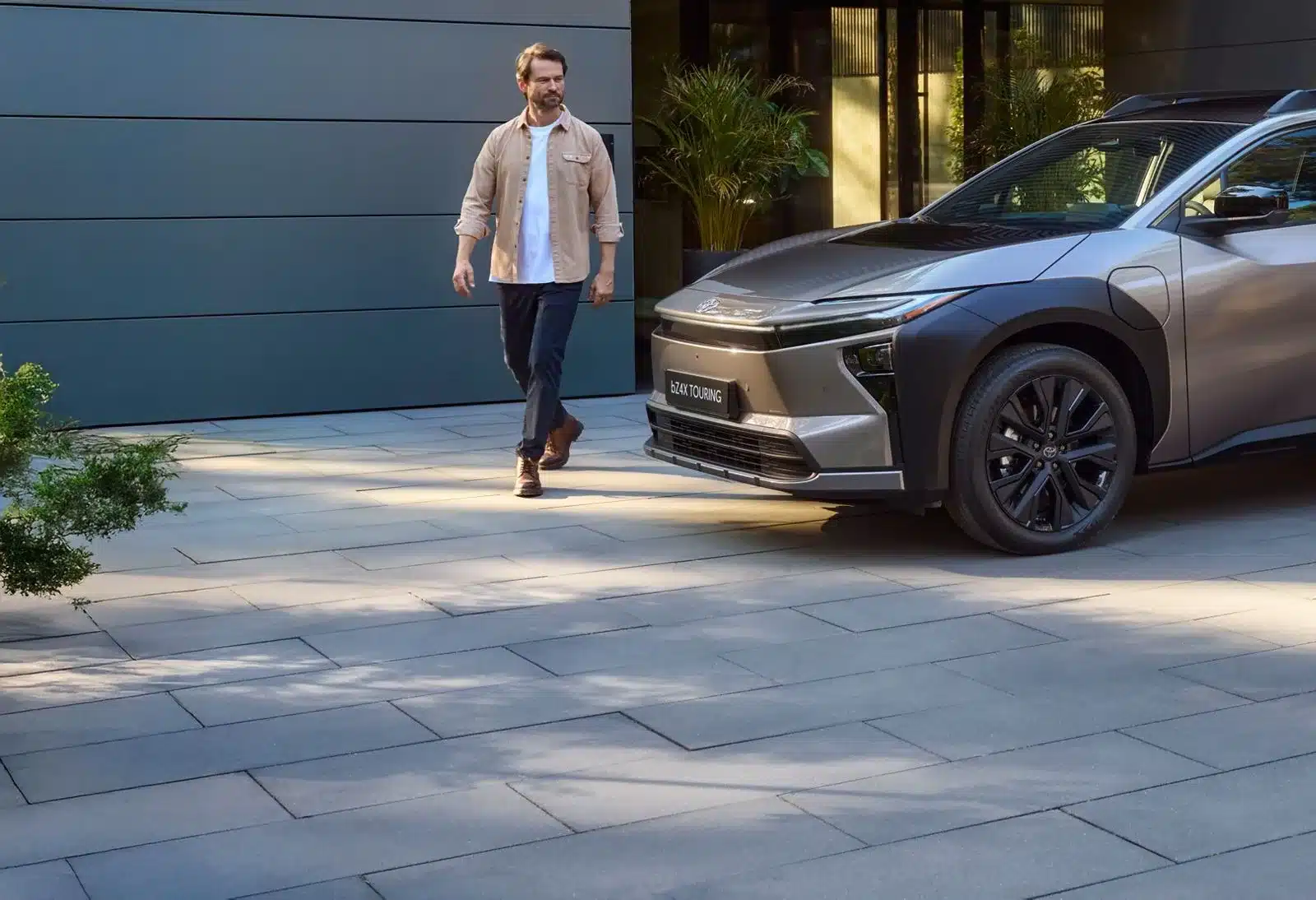 Toyota bZ4X Touring Elektro-SUV auf einer modernen Einfahrt mit Mann im Vordergrund