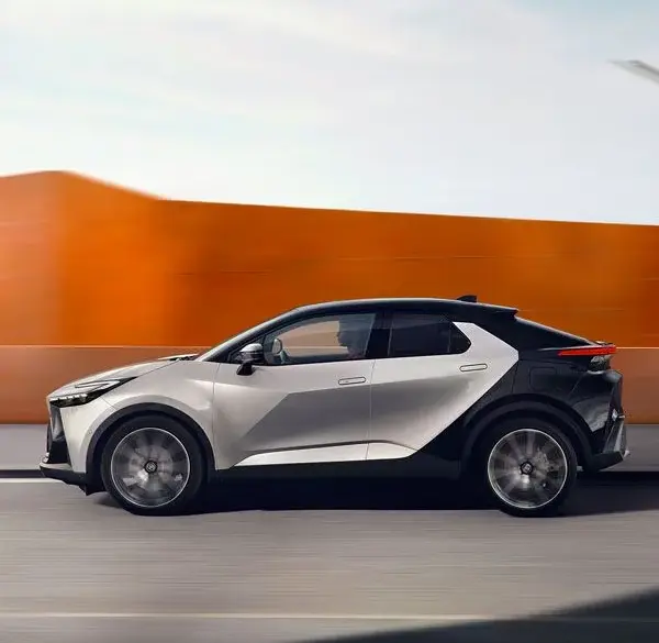 Toyota C-HR 2023 in Silber-Schwarz, seitlich fahrend vor moderner, orangefarbener Wand.