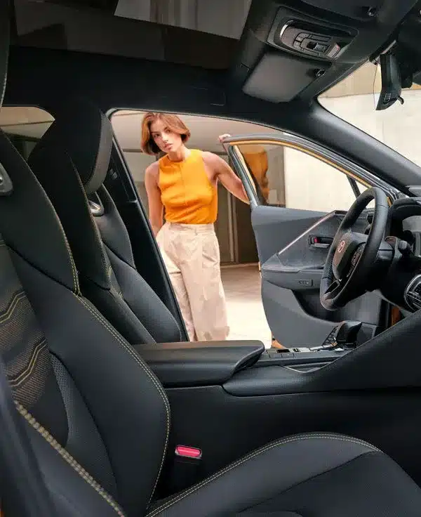 Innenansicht des Toyota C-HR+ mit geöffneter Tür und einer Frau, die von außen in das Fahrzeug blickt
