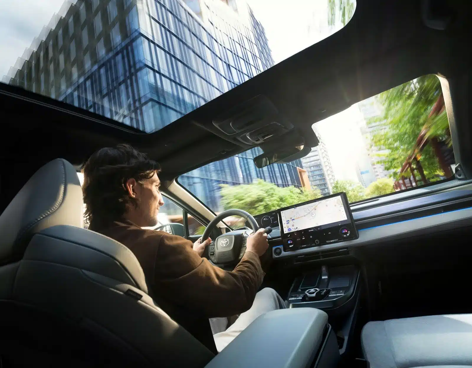 Fahrer steuert den Toyota C-HR+ mit großem Zentraldisplay und Panoramadach in urbaner Umgebung.