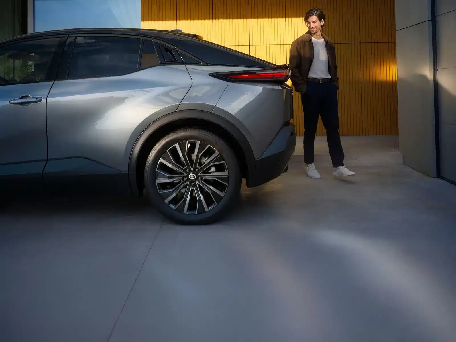 Toyota C-HR+ Elektro-SUV in Seitenansicht, ein Mann steht daneben in moderner Umgebung