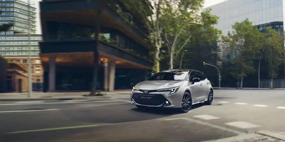 Toyota Corolla Hybrid, silber, fährt in moderner Stadtlandschaft.