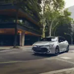 Toyota Corolla Hybrid, silber, fährt in moderner Stadtlandschaft.