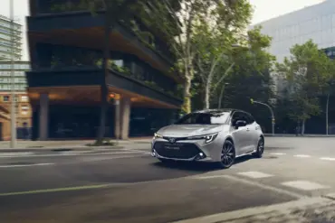 Toyota Corolla Hybrid, silber, fährt in moderner Stadtlandschaft.