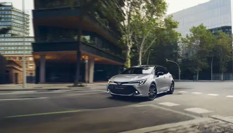 Toyota Corolla Hybrid, silber, fährt in moderner Stadtlandschaft.