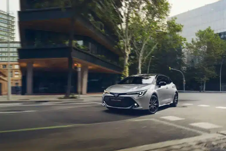 Toyota Corolla Hybrid, silber, fährt in moderner Stadtlandschaft.