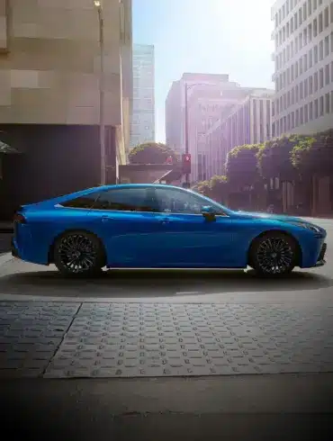 Seitenansicht des blauen Toyota Mirai, einer wasserstoffbetriebenen Limousine, in einer modernen Stadt.