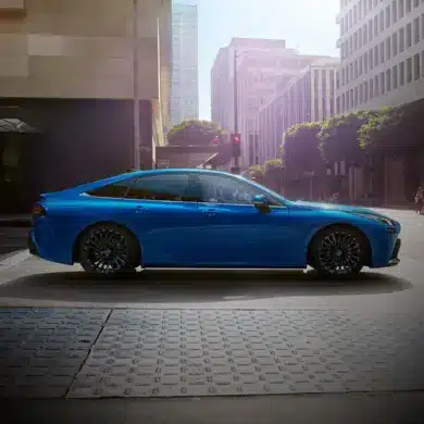 Seitenansicht des blauen Toyota Mirai, einer wasserstoffbetriebenen Limousine, in einer modernen Stadt.