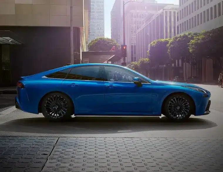 Seitenansicht des blauen Toyota Mirai, einer wasserstoffbetriebenen Limousine, in einer modernen Stadt.