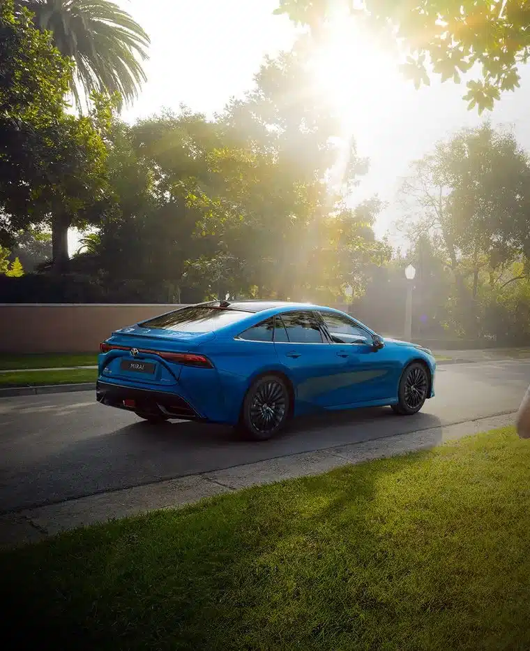 Blauer Toyota Mirai fährt an einem sonnigen Tag auf einer Baumallee