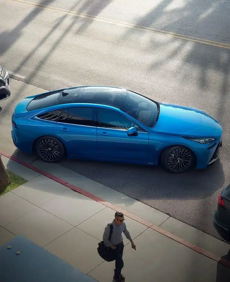 Blauer Toyota Mirai als Wasserstoff-Limousine, von oben fotografiert, parkend am Straßenrand.