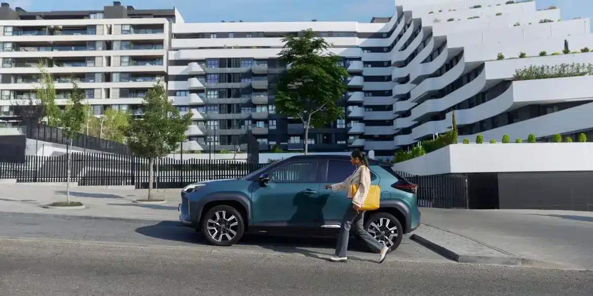 Frau geht auf einen Toyota Yaris Cross zu, der vor einer zeitgenössischen Wohnanlage parkt.