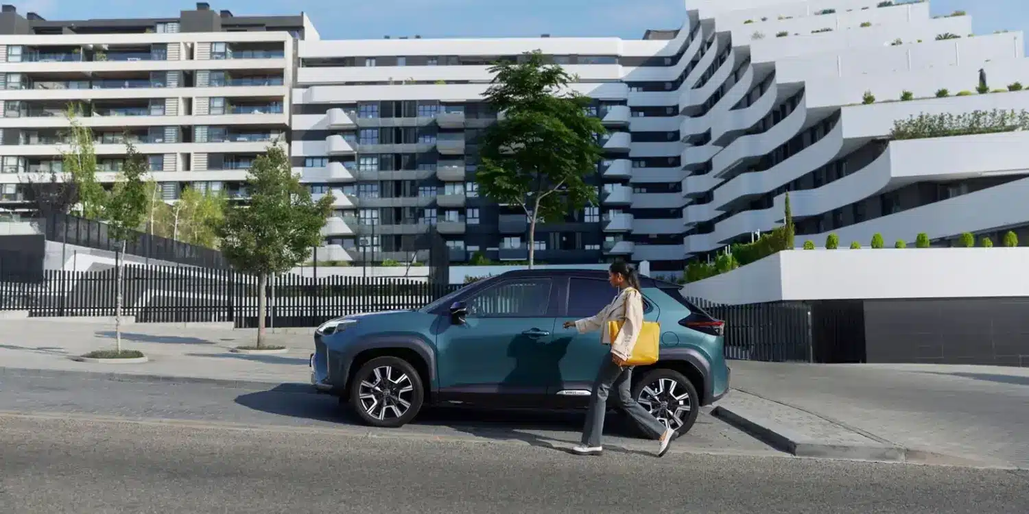 Frau geht auf einen Toyota Yaris Cross zu, der vor einer zeitgenössischen Wohnanlage parkt.