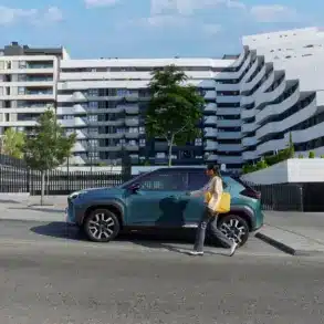 Frau geht auf einen Toyota Yaris Cross zu, der vor einer zeitgenössischen Wohnanlage parkt.