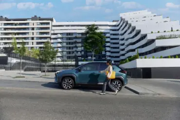 Frau geht auf einen Toyota Yaris Cross zu, der vor einer zeitgenössischen Wohnanlage parkt.