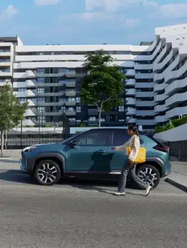 Frau geht auf einen Toyota Yaris Cross zu, der vor einer zeitgenössischen Wohnanlage parkt.