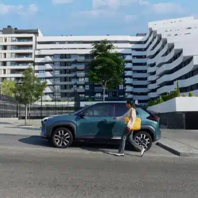 Frau geht auf einen Toyota Yaris Cross zu, der vor einer zeitgenössischen Wohnanlage parkt.