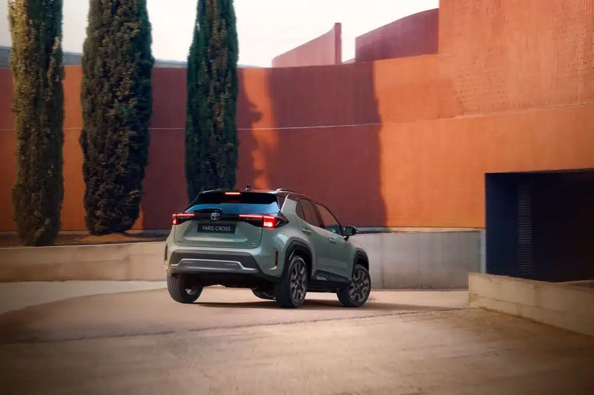 Toyota Yaris Cross von hinten, fährt entlang einer Mauer mit hohen Zypressen.