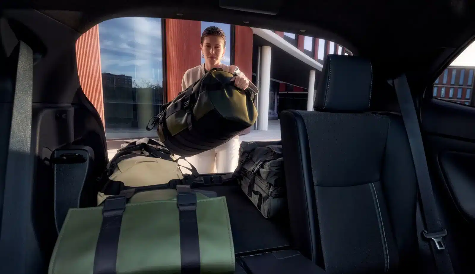 Blick in den Kofferraum eines Toyota Yaris Cross mit mehreren Reisetaschen und einer einladenden Person.