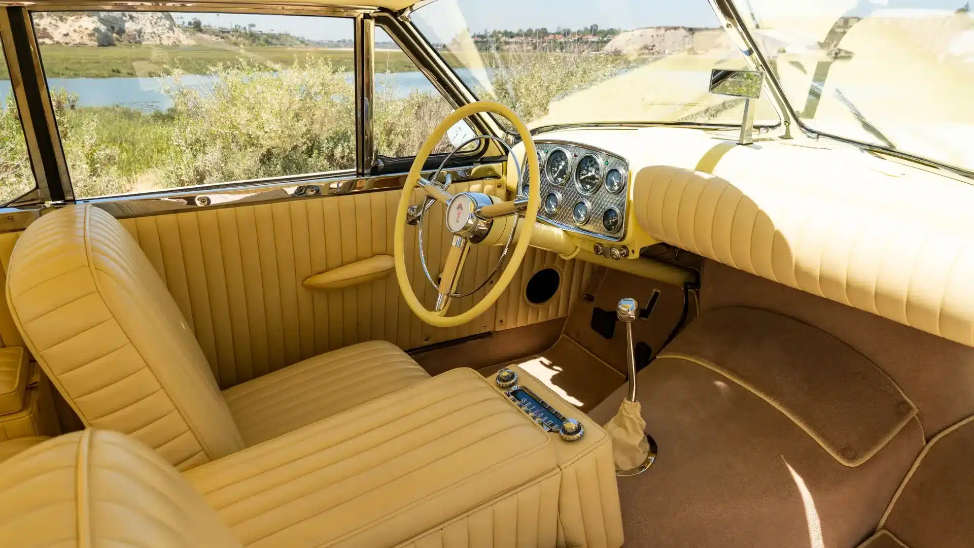 Detailaufnahme des cremefarbenen Innenraums eines 1952 Muntz Jet, mit Lenkrad, Armaturenbrett und Vordersitzen.