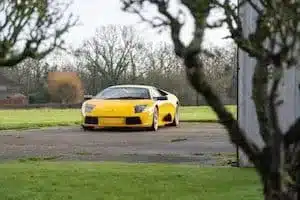 Gelber Lamborghini Murciélago 2002 auf einer Zufahrt, Bäume im Vordergrund