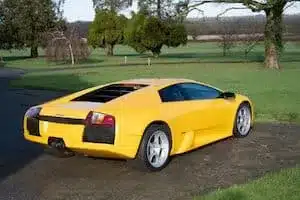 Gelber Lamborghini Murciélago 2002 von hinten auf einer Straße, mit aktiven Lufteinlässen und ikonischem Supersportwagendesign.
