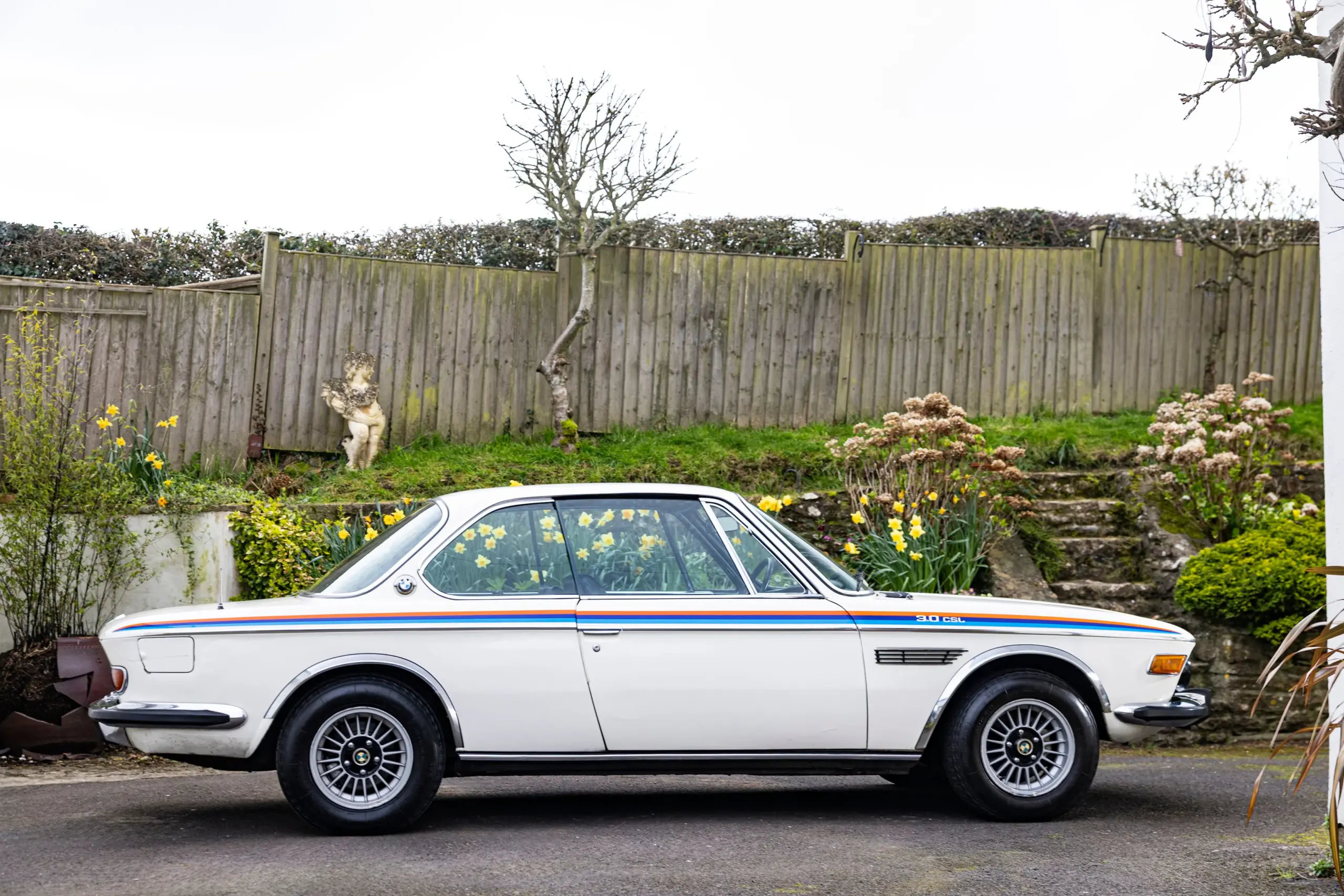 BMW 3.0 CSL von 1973, Coupé mit klassischen Motorsport-Elementen, seitlich aufgenommen, vor einem Garten.