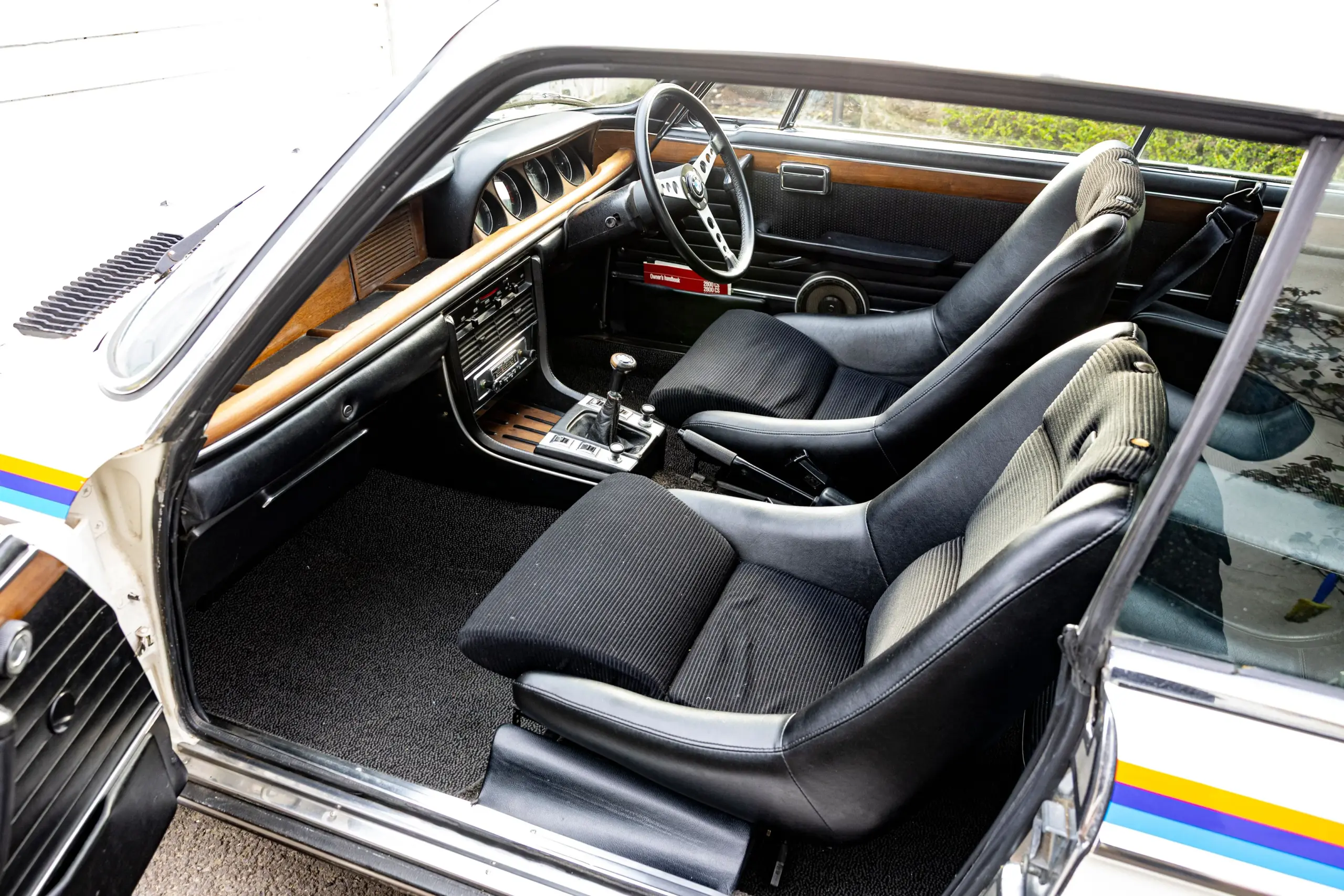 Blick auf das Interieur eines rechtsgelenkten BMW 3.0 CSL von 1973 mit Sportsitzen, Holzapplikationen und klassischem Armaturenbrett.