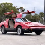 Bricklin SV-1, rotes Sportcoupé von 1975 mit offenen Flügeltüren auf einem Parkplatz, Seitenansicht.