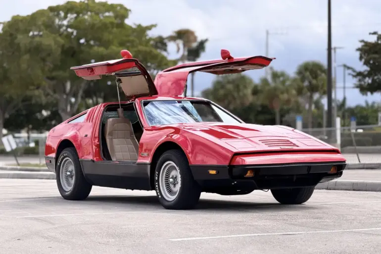 Bricklin SV-1, rotes Sportcoupé von 1975 mit offenen Flügeltüren auf einem Parkplatz, Seitenansicht.
